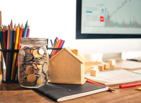 How to start investing for beginners concept with coins in a glass jar, small house model, financial notebook, and stock market chart on computer screen in a realistic workspace setup.