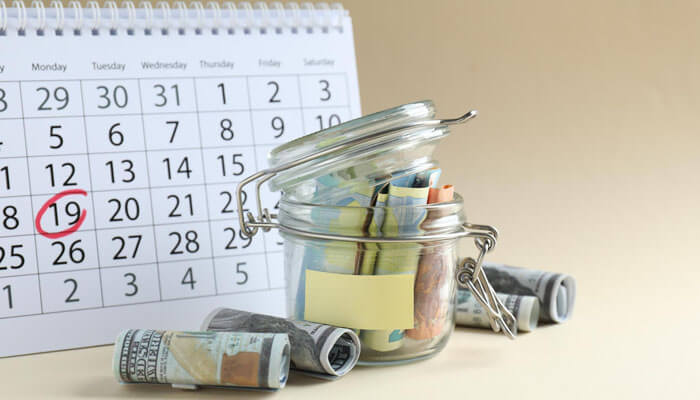 Starting small and investing consistently concept with cash savings in a glass jar, calendar reminder marked for regular contributions, and budgeting plan in a realistic setup.